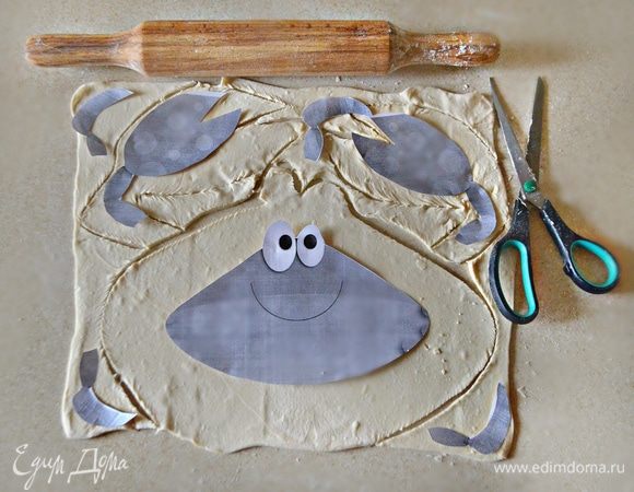 Слоеное дрожжевое тесто разморозьте при комнатной температуре. Немного раскатайте, посыпав поверхность мукой, и вырежьте с помощью шаблона крабика (по 2 шт каждой его составляющей).