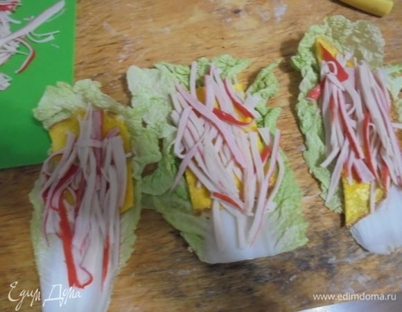 Для рулетиков разложить листья пекинской капусты, по 1 кусочку омлета, слой крабовых палочек и слой огурцов. Смажьте соусом, сверните в рулетики.