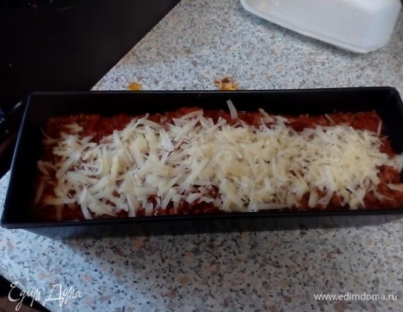 Последние листы смазать соусом «Бешамель», далее выложить томатно-мясную базу и верх густо засыпать тертым сыром пармезан.