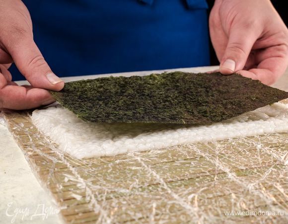 Смочив руки в смеси тэдзу, возьмите коврик положите сверху рис и разровняйте, образуя прямоугольник. Сверху положите нори.
