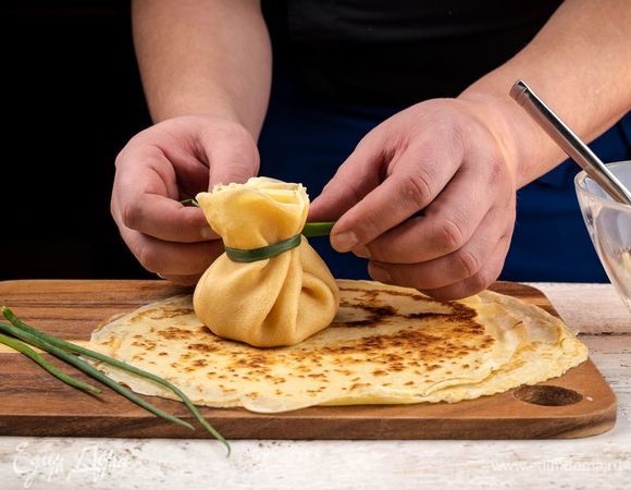 В центр каждого блинчика положите начинку, соберите блинчик в форме мешочка и перевяжите пером зеленого лука. 