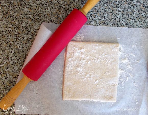 Тесто размораживаем при комнатной температуре, чтобы его можно было раскатать. 
Кладем его на бумагу для выпечки, присыпанную немного мукой. Тесто сверху также посыпаем мукой, чтобы оно не прилипало к скалке. Раскатываем скалкой прямоугольник толщиной 0,5 см. Перекладываем его на стол, также немного посыпанный мукой. Бумага нам еще пригодится. 
