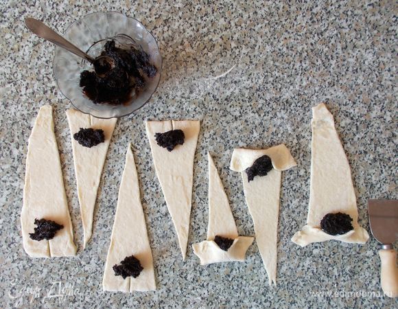 Берем готовую маковую начинку с шоколадом, по форме она напоминает «колбаску». Делаем в «колбаске» с шоколадной маковой начинкой надрез и выдавливаем ее в вазочку. Пахнет очень приятно. Не удержалась, попробовала ее так. Оказалась очень вкусная и без выпечки. Чайной ложкой выкладываем маковую начинку на широкую сторону каждого получившегося треугольничка.  Сворачиваем наши круассаны.
Обратите внимание, что для придания круассану красивой формы на основании каждого треугольничка я делаю надрез, чтобы края можно было растянуть в стороны, тем самым удлинив наши круассаны. Если вы используете какую-то другую начинку (или готовите ее сами), прижмите хорошо уголки теста, чтобы начинка не вытекла.
