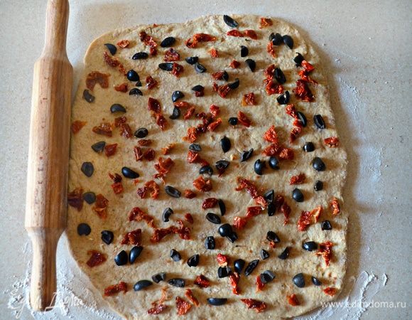 Вяленые томаты и маслины нарежьте мелкими кусочками. Я использовала 10 шт. роскошных крупных сицилийских вяленых томатов, замочив их предварительно на 20 мин. в теплую подсоленную воду и затем промокнув бумажными полотенцами. В том случае, если у вас вяленые томаты в масле, то замачивать их, конечно же, не нужно))
Подготовленное тесто раскатайте на присыпанной мукой поверхности в пласт, распределите на поверхности кусочки томатов и маслин. Затем сверните рулетом, перенесите на противень, выстеленный пергаментом и смазанный растительным маслом. На поверхности рулета сделайте косые надрезы ножом, накройте чистым полотенцем и дайте немного подняться, в течение 15-20 мин. 