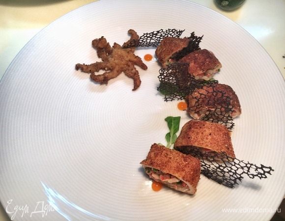 Выложите кусочки кальмара и щупальце на тарелку. При помощи листиков корна можно создать устойчивость. Поломайте тюили на «лепестки» и зафиксируйте их между кусочками. В свободном порядке нанесите капельки острого соуса на тарелку рядом с кальмаром.
