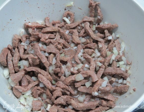 В большую сковороду налить растительное масло, сковороду хорошо нагреть и на сильном огне обжарить мясо. Затем добавить нарезанный лук, огонь убавить до среднего.