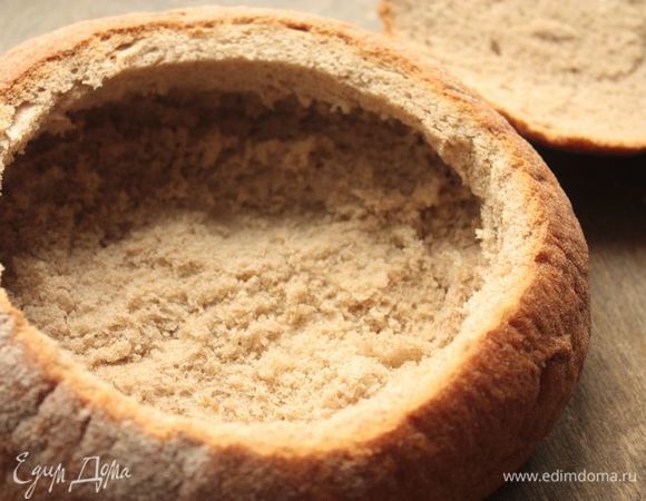 Для подачи вам понадобится круглая буханка хлеба: ищите среднего размера, чтобы она вместила в себя не больше одной порции супа. Срежьте верхний слой буханки, это будет наша крышечка. Аккуратно удалите часть хлебного мякиша, оставив при этом толстые стенки и толстое дно (иначе хлеб впитает суп и размякнет, потеряв форму). Отправьте хлеб в духовку, разогретую до 250°С, на 5-7 минут, чтобы он лучше схватился.