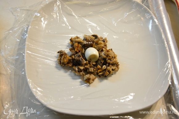 Расстелить пищевую пленку на тарелку или разделочную доску, сверху выложить 2 ст. л. грибной начинки и в середину положить перепелиное яйцо.