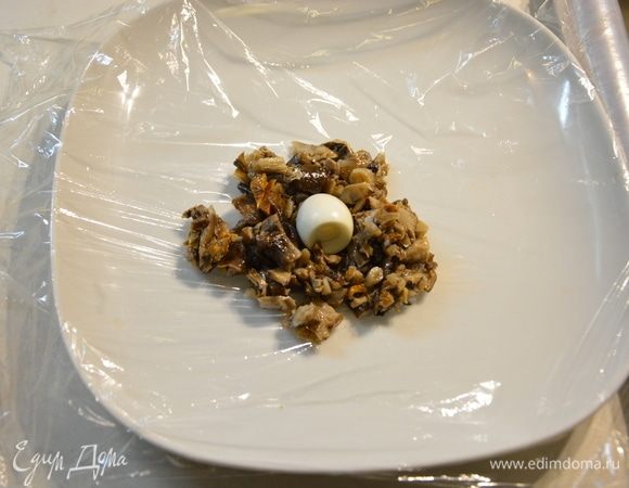 Расстелить пищевую пленку на тарелку или разделочную доску, сверху выложить 2 ст. л. грибной начинки и в середину положить перепелиное яйцо.