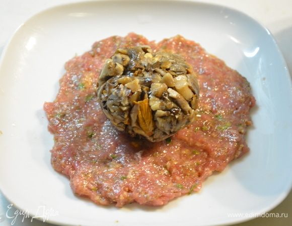 Смазать тарелку растительным маслом или смочить холодной водой. Расстелить на тарелке круг из 1/4 части фарша. Сверху положить грибной шарик. Смочить руки холодной водой, перевернуть тарелку на ладонь, аккуратно придерживая грибной шарик. Фарш сойдет с тарелки и покроет шарик. 