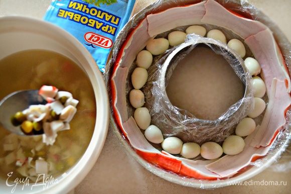 Выложить порезанные яйца на дно формы. К бульону добавьте по 3 ст. л. консервированной кукурузы, зеленого горошка и порезанную белую часть крабовых палочек. Перемешать.