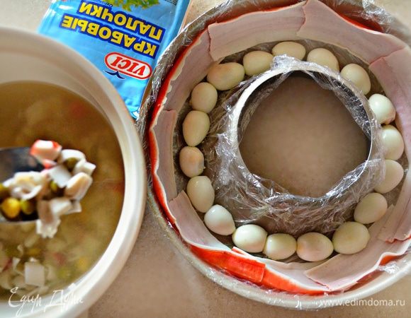 Выложить порезанные яйца на дно формы.
К бульону добавьте по 3 ст. л. консервированной кукурузы, зеленого горошка и порезанную белую часть крабовых палочек. Перемешать. 