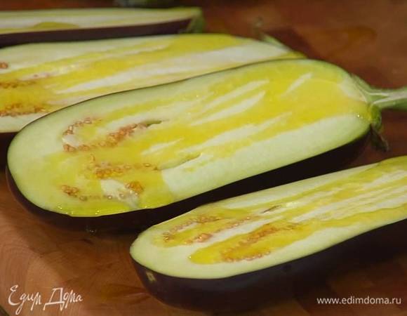 Баклажаны разрезать вдоль пополам, сбрызнуть 2 ст. ложками оливкового масла, выложить на выстеленный бумагой для выпечки противень срезами вверх и запекать под разогретым грилем 20 минут.