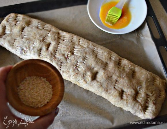 Заверните края и сверните рулетом. Аккуратно уложите рулет швом вниз на покрытый пекарской бумагой и смазанный растительным маслом противень. Вилкой сделайте наколы. Смажьте поверхность штруделя желтком и обильно посыпьте кунжутом.