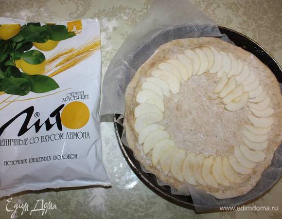 Тесто следует аккуратно выложить на присыпанный мукой стол. Возьмем ¾ теста и раскатаем круг. Это послужит основанием для пирога. Переложим его в форму, выстланную пергаментной бумагой. Нарежем яблоки чешуйкой, выложим на тесто. 