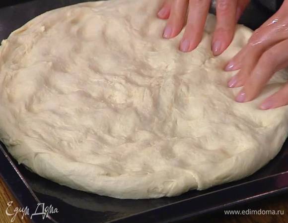 Подошедшее тесто вымесить, так чтобы оно получилось воздушным и отлипало от рук, переложить его на противень и сформировать круглую тонкую лепешку.