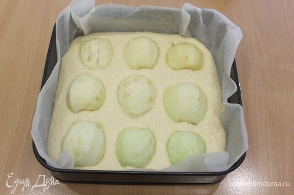 Форму 24 на 24 см застелить бумагой, выложить тесто, половинки очищенных яблок выложить на тесто, слегка вдавив в тесто. Выпекать при 190°С 30–35 минут.