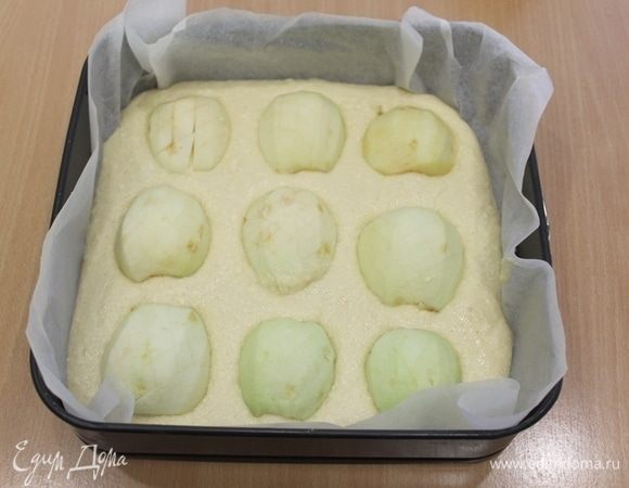 Форму 24 на 24 см застелить бумагой, выложить тесто, половинки очищенных яблок выложить на тесто, слегка вдавив в тесто. Выпекать при 190°С 30–35 минут.