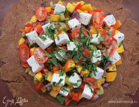 На пергаменте или силиконовом коврике раскатать охлажденное тесто. С помощью тарелки подходящего диаметра наметить контур для начинки. Выложить начинку, сверху разместить нарезанные на половинки помидоры черри, кубики феты и рубленую зелень (у меня петрушка).