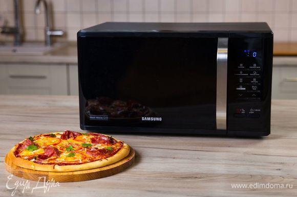 Готовую пиццу в горячем виде еще раз посыпьте оставшимся тертым сыром и украсьте зеленью. Аппетитное блюдо готово!