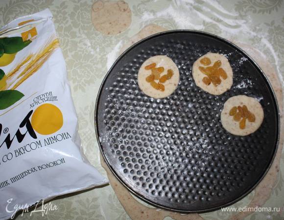 На противень, посыпанный мукой, выкладываем основание. Сверху кладем немного изюма. 