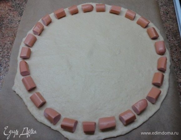 Тесто раскатать на бумаге для выпечки в круг и разложить по краю кусочки сосисок. Можно поближе, чем у меня, оставляя не боле 0,5 см между кусочками.