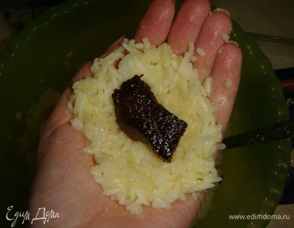 Берем столовую ложку риса, утрамбовываем его в руке в форме лепешки, кладем кусочек мяса, сверху еще немного риса и формируем шарик, прижимая рис руками. После каждого колобка смачиваем руки в воде. 