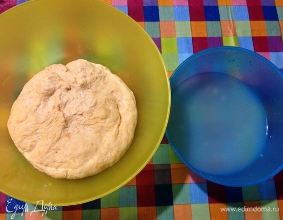 Теперь такой интересный момент, как из него, такого нежного и непослушного, слепить булочки. Скатать у меня не получалось, рассказываю, как я делала.
Ставлю рядом с миской теста миску с водой, обмакиваю руки в воду, затем оттягивая шматок теста одной рукой, второй рукой его отщипываю как ножницами и этот шматок не скатываю в колобок, а делаю так.
В левой держу кусочек теста, правой рукой пальцами как бы подкручиваю края теста под низ к нижнему центру и так двигаюсь по кругу, проделываю это, повторюсь, мокрыми руками, обмакивая руки в воду перед каждым кусочком теста. Выходит такой колобок.