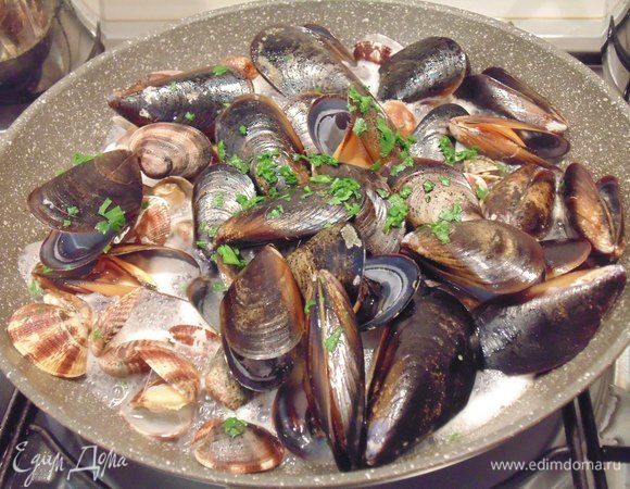 В сковороде разогреть 2 ст. ложки оливкового масла, добавить дольку чеснока, обжарить чеснок и затем его выкbнуть. Выложить морепродукты, влить вино, посыпать петрушкой, накрыть крышкой, дать раковинам открыться.