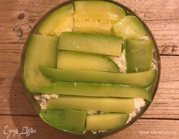 В круглую глубокую чашку выложить внахлест кабачковые слайсы по кругу. Заполнить начинкой, закрыть оставшимися кабачками. Накрыть плоской тарелкой и охладить в течение 4–5 часов. Идеально оставить на ночь.