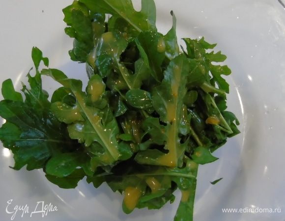 Руколу помойте и обсушите. Выложите в салатник, полейте половиной заправки.
