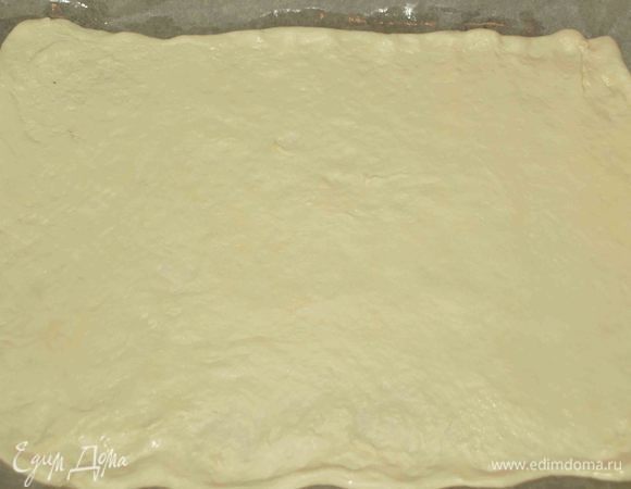 Заранее размороженное тесто делим на две части. Оставляя для основы пирога большую часть. Раскатываем большую часть и выкладываем на противень, застеленный пекарской бумагой, смазанной растительным маслом. Распределяем тесто по противню. 