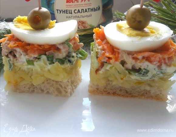 Собираем салат. В форму кладем хлеб, на него слой из картофеля и смазываем майонезом. Далее нужно выложить слой зеленого лука, а сверху — консервированный тунец ТМ «Магуро». Также смазываем майонезом. Следующим шагом кладем морковь, смазываем майонезом и украшаем кружочком яйца и оливками.