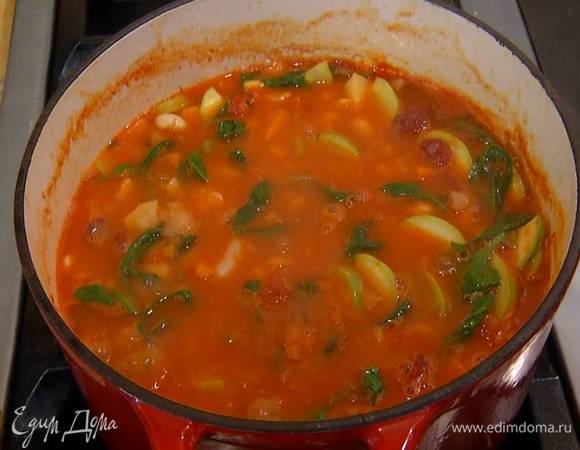Когда бульон закипит, добавить помидоры в собственном соку, отваренную фасоль, нарезанный кабачок и готовить минут семь, затем посолить, отправить в суп измельченный руками пеперончино, шпинат, охотничьи колбаски и еще немного подержать на огне.