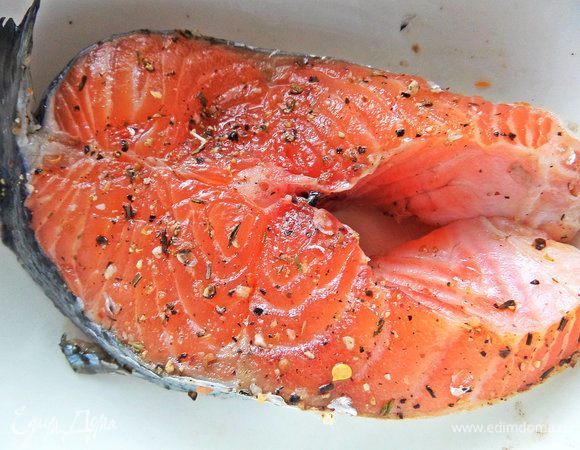 Обсыпать заранее большой лососевый стейк лимонным перцем, солью и ароматными травами. Накрыть и убрать в холодильник.
