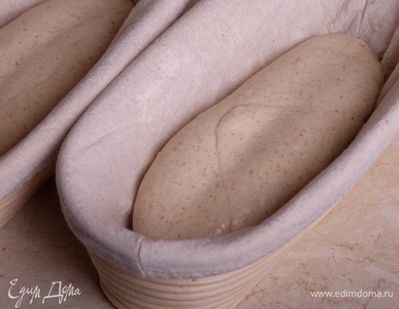 Тонкой деревянной скалкой, подпыленной мукой, продавить вмятину вдоль заготовки, поместить в расстоечную корзинку швом вверх (не вмятиной!) и поставить на расстойку на 2 часа. За это время заготовки должны увеличиться в объеме.