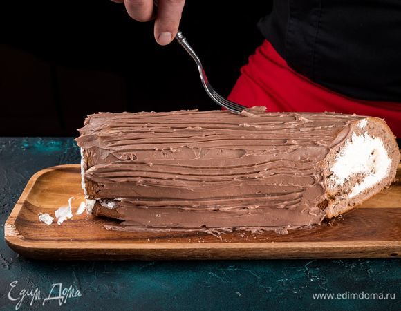 Отрежьте спереди и сзади наискосок небольшие куски рулета. Смажьте рулет кремом, оставив нетронутыми края. Сделайте узоры вилкой на полене. 