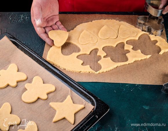 С помощью разных формочек вырежьте из теста фигурки: звездочки, человечков, снеговиков, елки. Противень застелите пергаментом, выложите на него заготовки печенья. Выпекайте в духовке 15 минут при 180°С.