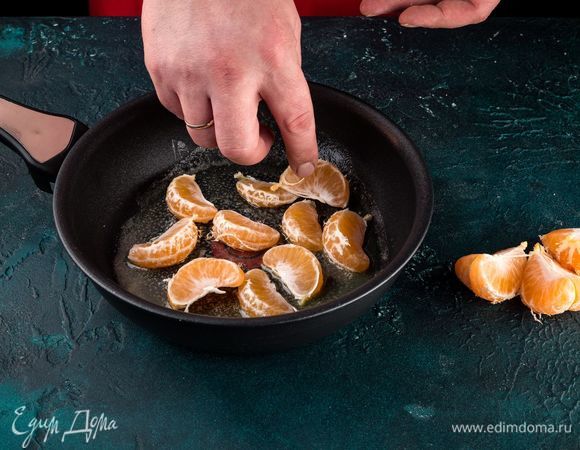 Когда мандариновые дольки подсохнут, в сковороде разогрейте немного масла, посыпьте его ложкой сахара и добавьте мандарины. Цитрусы обжарьте с двух сторон по 2 минуты.