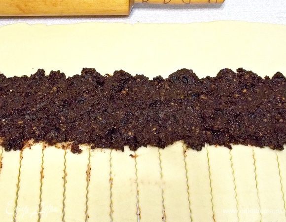 Раскатать тесто в прямоугольник и виртуально разметить его на 3 части по длине. Верхнюю часть не тронуть, на среднюю положить и разровнять половину начинки. Последнюю часть при помощи ролика для пиццы разрезать на полоски.