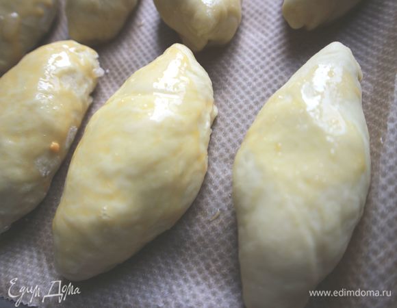 Положить пирожки швом вниз на противень, покрытый бумагой для выпечки. Дать постоять 10 минут, смазать кисточкой смесью желтка и молока. 