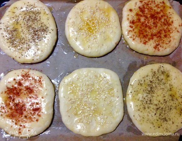 Так как у меня противни небольшого размера от электропечи, то у меня все лепешки не поместились, осталось еще 4 лепешки, их я положила на рабочую доску, слегка посыпанную мукой. Все лепешки разложены, оба противня и рабочую доску накрываем полотенцами и даем расстояться еще 30–40 минут.
Духовку тем временем включаем на 200°С.
Время прошло, лепешки расстоялись и увеличились в объеме.
Теперь смазываем растопленным сливочным маслом все лепешки по мере их становления в духовку. Смазываем лепешки с первого противня и посыпаем их разными посыпками, как на фото: кунжутом, базиликом, паприкой+розмарин. Отправляем первый противень в уже горячую духовку на 20 минут.
