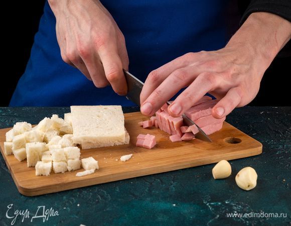 Нарежьте хлеб кубиками и слегка подсушите в духовке. Нарежьте кубиками ветчину. Измельчите чеснок.