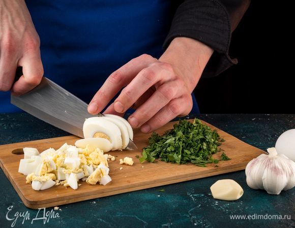 Отварите яйца и порубите кубиками. Нашинкуйте зелень и измельчите чеснок.