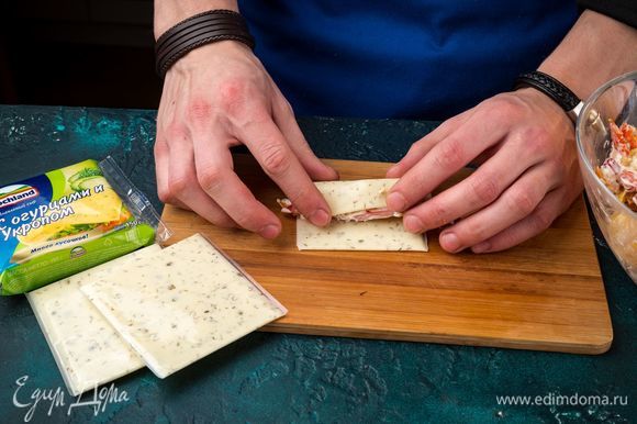 Выложите по 1–2 ч. л. начинки на ломтик плавленого сыра Hochland, сверните рулетики.