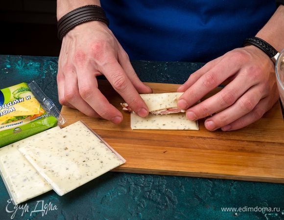 Выложите по 1–2 ч. л. начинки на ломтик плавленого сыра Hochland, сверните рулетики.