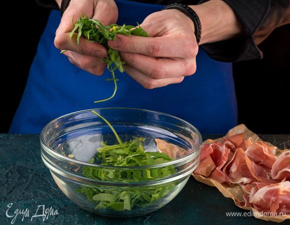 Нарежьте прошутто очень тонкими широкими ломтиками. Пучок руколы порвите руками.