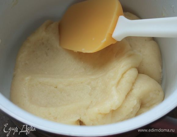 Как только смесь закипит, всыпьте в нее просеянную муку и начните интенсивно мешать, пока тесто будем собирать в однородный ком. Убавьте огонь до медленного (сотейник с огня не снимайте) и продолжайте тщательно вымешивать тесто с помощью лопатки в течение 3–4 минут. Наша задача — не дать тесту прилипнуть к стенкам сотейника, но дать ему дойти до нужного состояния. Как только на дне сотейника образуется тонкая пленочка из теста, можно снимать сотейник с огня и оставлять остывать.