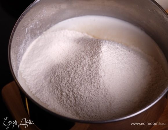 Соединить вместе оба вида муки. Сотейник снять с огня и просеять в молочную смесь муку.