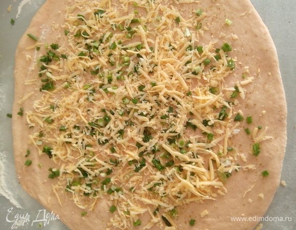 Расстоявшееся тесто обминаем и раскатываем не очень тонко. Посыпаем измельченным луком и сыром тертым на крупной терке.